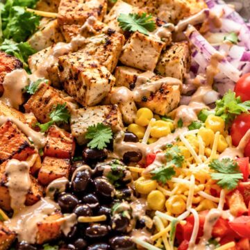 Tex-Mex chicken sweet potato bowl with grilled chicken, roasted sweet potatoes, black beans, corn, tomatoes, red onion, shredded cheese, romaine, cilantro, and creamy sauce.