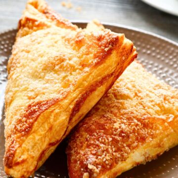 Close-up of two crisp, golden-brown air fryer apple turnovers stacked on a plate.