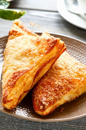Close-up of two crisp, golden-brown air fryer apple turnovers stacked on a plate.