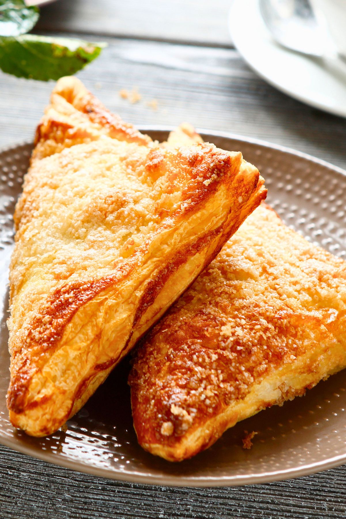 Close-up of two crisp, golden-brown air fryer apple turnovers stacked on a plate.