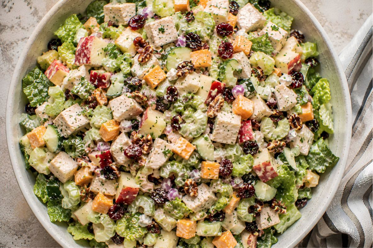 Apple cheddar chicken chopped salad with romaine, chicken breast, cheddar cheese, apples, celery, cucumber, red onion, dried cranberries, pecans, and creamy dressing in a large bowl.