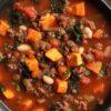 Close-up of hearty beef and sweet potato soup with ground beef, diced sweet potatoes, white beans, kale, tomatoes, and vegetables in a rich tomato broth.