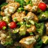 High protein chicken rice bowl with seasoned chicken breast, brown rice, broccoli, spinach, avocado, cherry tomatoes, green onions, and creamy dressing in a black bowl.