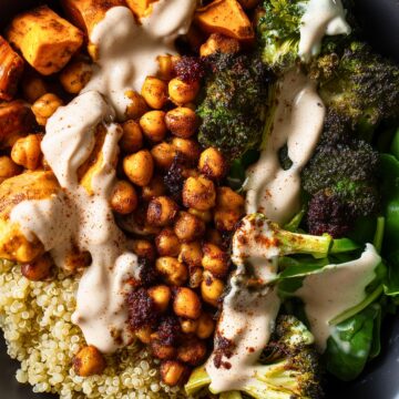 Chickpea Sweet Potato Protein Bowl with roasted sweet potatoes, crispy chickpeas, broccoli, quinoa, and fresh spinach in a black bowl, topped with a creamy sauce.