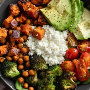 Cottage cheese sweet potato bowl with roasted sweet potatoes, crispy chickpeas, broccoli, cherry tomatoes, spinach, sliced avocado, and a generous scoop of creamy cottage cheese in a black bowl.