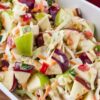 Crunchy apple coleslaw with chunks of green and red apples, shredded cabbage and carrots, diced red bell pepper, and sliced green onion tossed in a creamy dressing and served in a white dish.