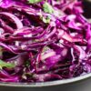 Crunchy red cabbage lime slaw with thinly sliced purple cabbage, red onion, and fresh cilantro tossed in a light lime dressing and served in a black bowl.