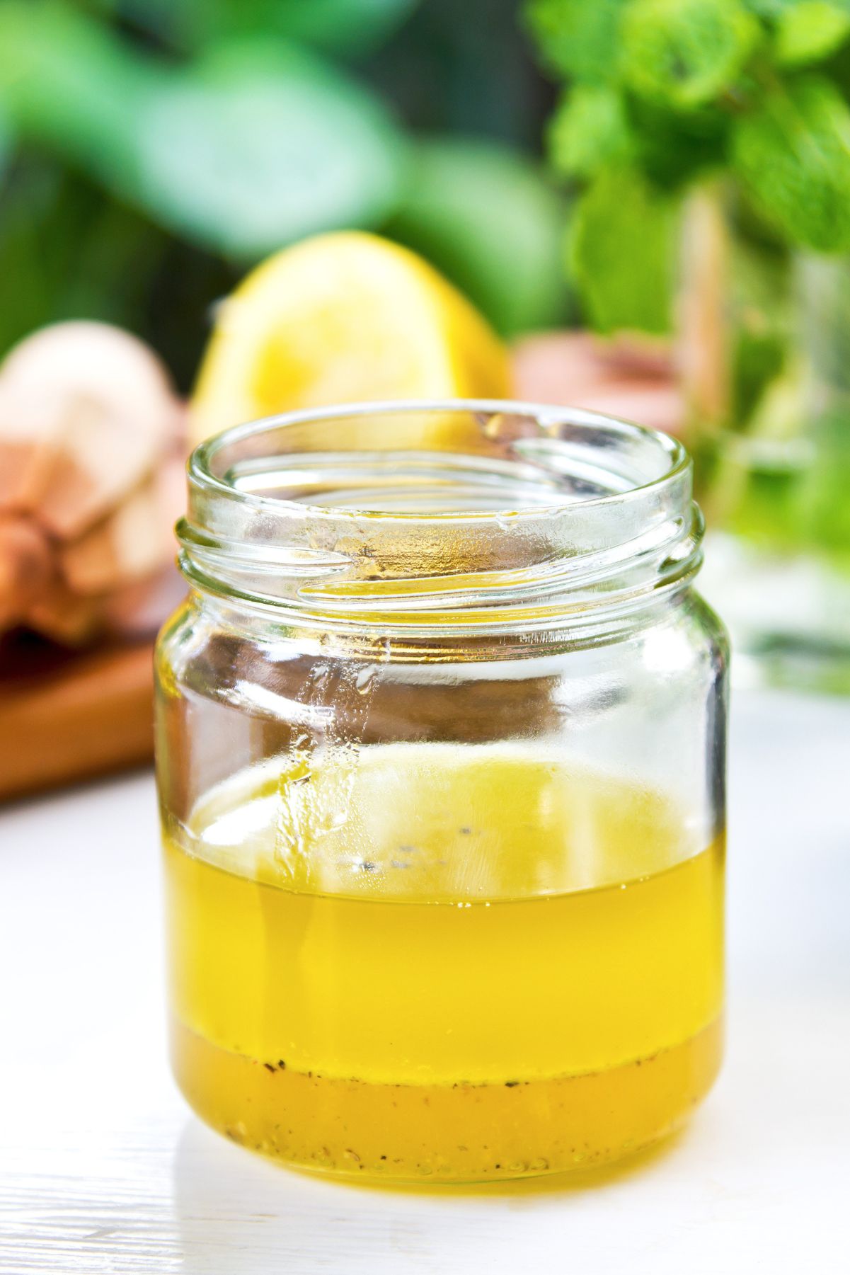Fresh lemon garlic vinaigrette in a clear glass jar with golden dressing and black pepper, with a lemon, garlic bulb, and fresh herbs softly blurred in the background.