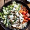 Garlic herb chicken and brown rice bowl with romaine, cucumber, carrots, cherry tomatoes, parsley, and creamy yogurt sauce, served with extra dressing and lemon.