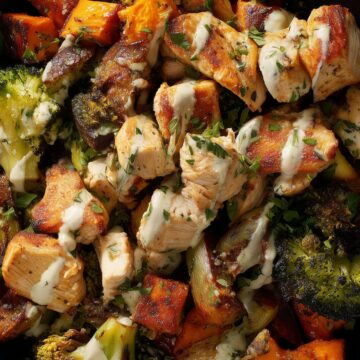 Garlic Parmesan chicken sweet potato bowl with roasted chicken breast, sweet potato chunks, broccoli, herbs, and creamy Parmesan sauce in a black bowl.