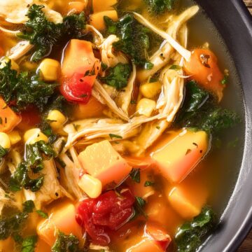 Close-up of harvest chicken vegetable soup with shredded chicken, sweet potatoes, kale, corn, and tomatoes in golden broth.