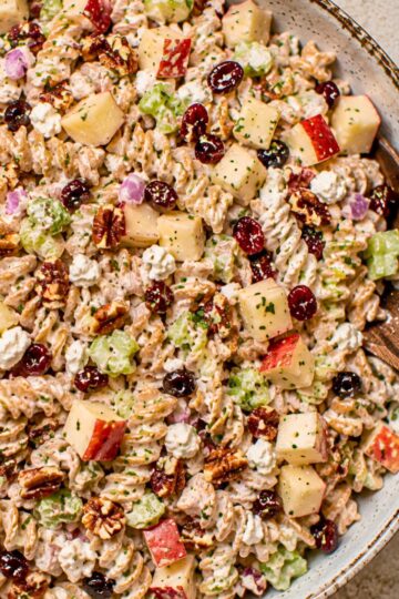Creamy healthy apple pecan pasta salad with whole wheat rotini, chopped red apples, celery, dried cranberries, pecans, red onion, feta cheese, and herbs in a creamy dressing.