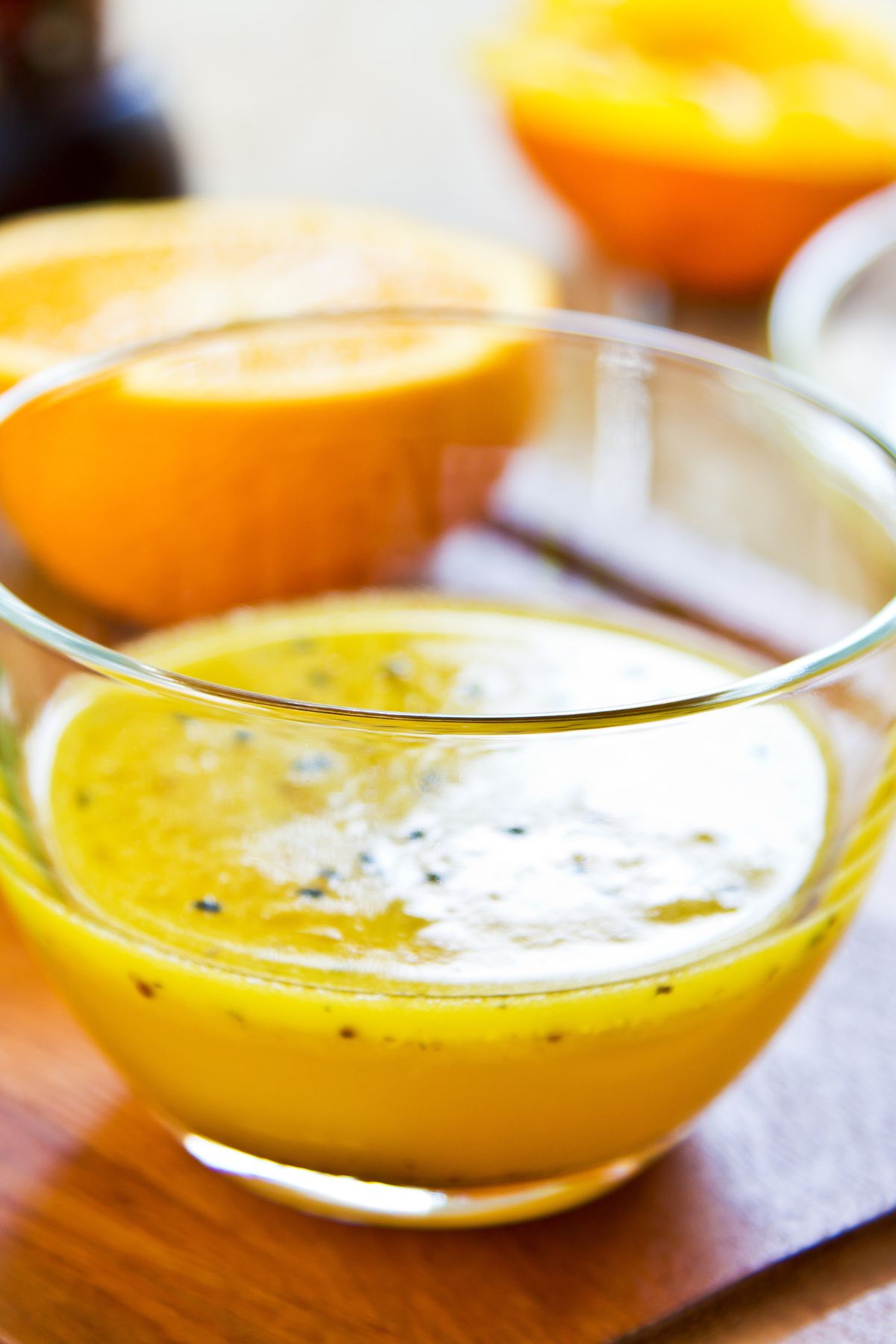 Close-up of homemade orange black sesame vinaigrette in a clear glass bowl, with fresh orange halves in the background.