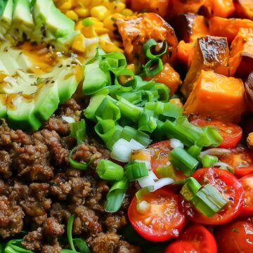 Hot honey beef sweet potato bowl with seasoned ground beef, roasted sweet potatoes, avocado, corn, spinach, cherry tomatoes, and sliced green onions in a black bowl.