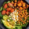 Hot honey cottage cheese sweet potato bowl with roasted sweet potatoes, seasoned chickpeas, baby spinach, cherry tomatoes, avocado, green onions, and cottage cheese, finished with a sweet and spicy honey drizzle.