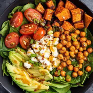 Hot honey cottage cheese sweet potato bowl with roasted sweet potatoes, seasoned chickpeas, baby spinach, cherry tomatoes, avocado, green onions, and cottage cheese, finished with a sweet and spicy honey drizzle.