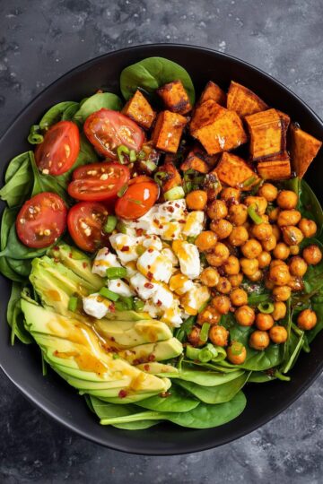 Hot honey cottage cheese sweet potato bowl with roasted sweet potatoes, seasoned chickpeas, baby spinach, cherry tomatoes, avocado, green onions, and cottage cheese, finished with a sweet and spicy honey drizzle.