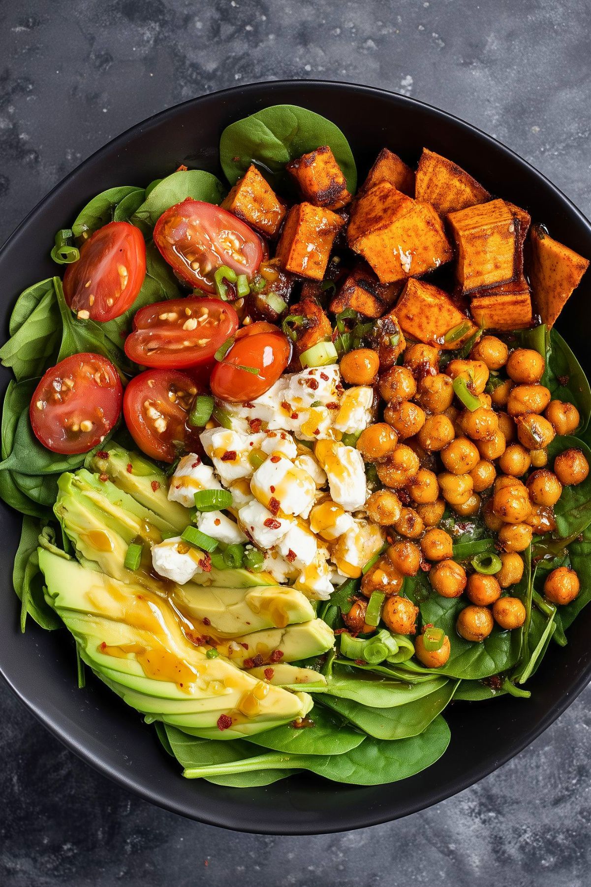 Hot honey cottage cheese sweet potato bowl with roasted sweet potatoes, seasoned chickpeas, baby spinach, cherry tomatoes, avocado, green onions, and cottage cheese, finished with a sweet and spicy honey drizzle.