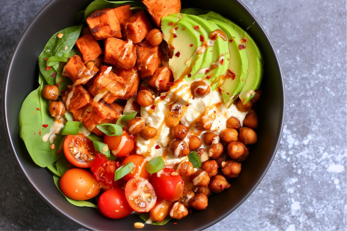 Hot honey cottage cheese sweet potato bowl with roasted sweet potatoes, seasoned chickpeas, cottage cheese, avocado, baby spinach, cherry tomatoes, and green onions, drizzled with hot honey and red pepper flakes.