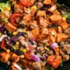High protein hot honey turkey sweet potato bowl with ground turkey, roasted sweet potatoes, black beans, corn, tomatoes, red onion, lettuce, and creamy sauce in a black bowl.