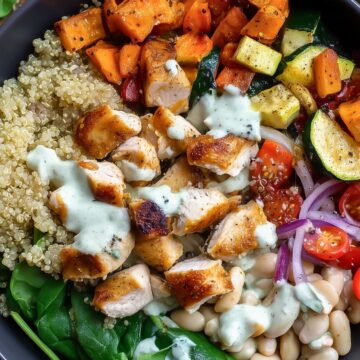 Italian chicken sweet potato bowl with roasted chicken, sweet potatoes, quinoa, zucchini, white beans, spinach, cherry tomatoes, red onion, and creamy dressing in a black bowl.