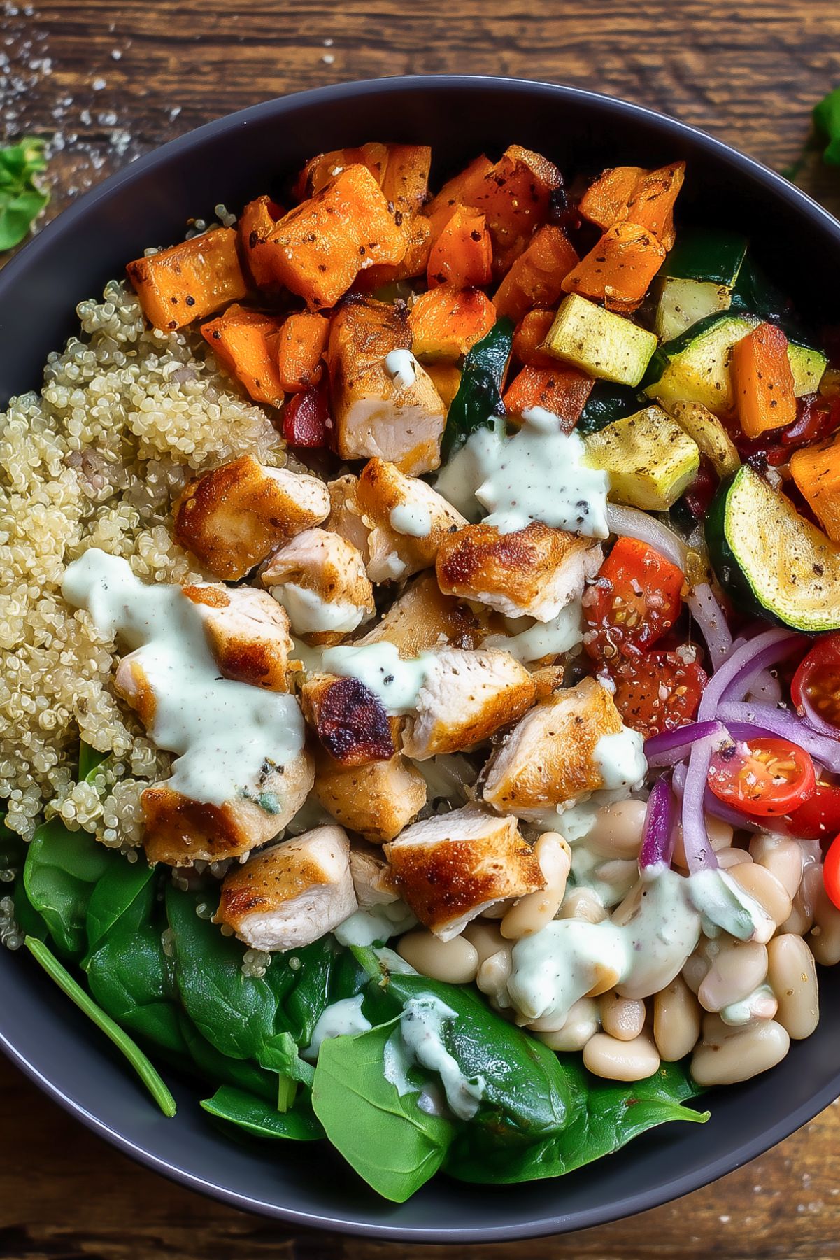 Italian chicken sweet potato bowl with roasted chicken, sweet potatoes, quinoa, zucchini, white beans, spinach, cherry tomatoes, red onion, and creamy dressing in a black bowl.