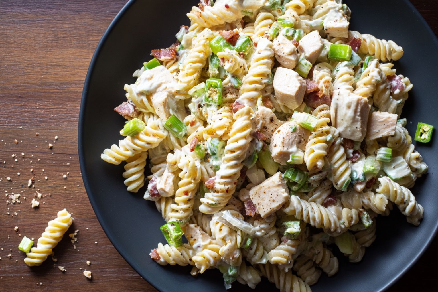 High protein jalapeño popper chicken pasta salad with rotini, chunks of chicken breast, turkey bacon, chopped green onions, jalapeños, and creamy dressing served on a matte black plate.
