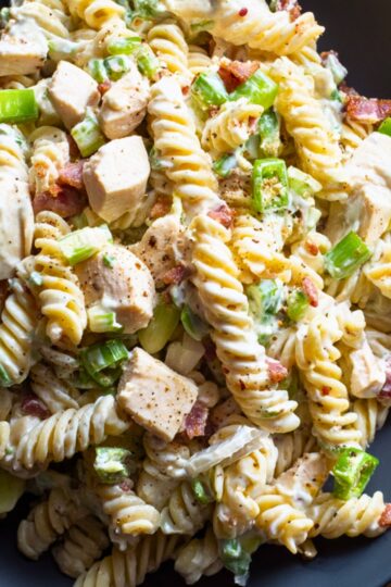 Close-up of high protein jalapeño popper chicken pasta salad with rotini, chunks of chicken breast, turkey bacon, green onions, jalapeños, and creamy dressing with black pepper seasoning.