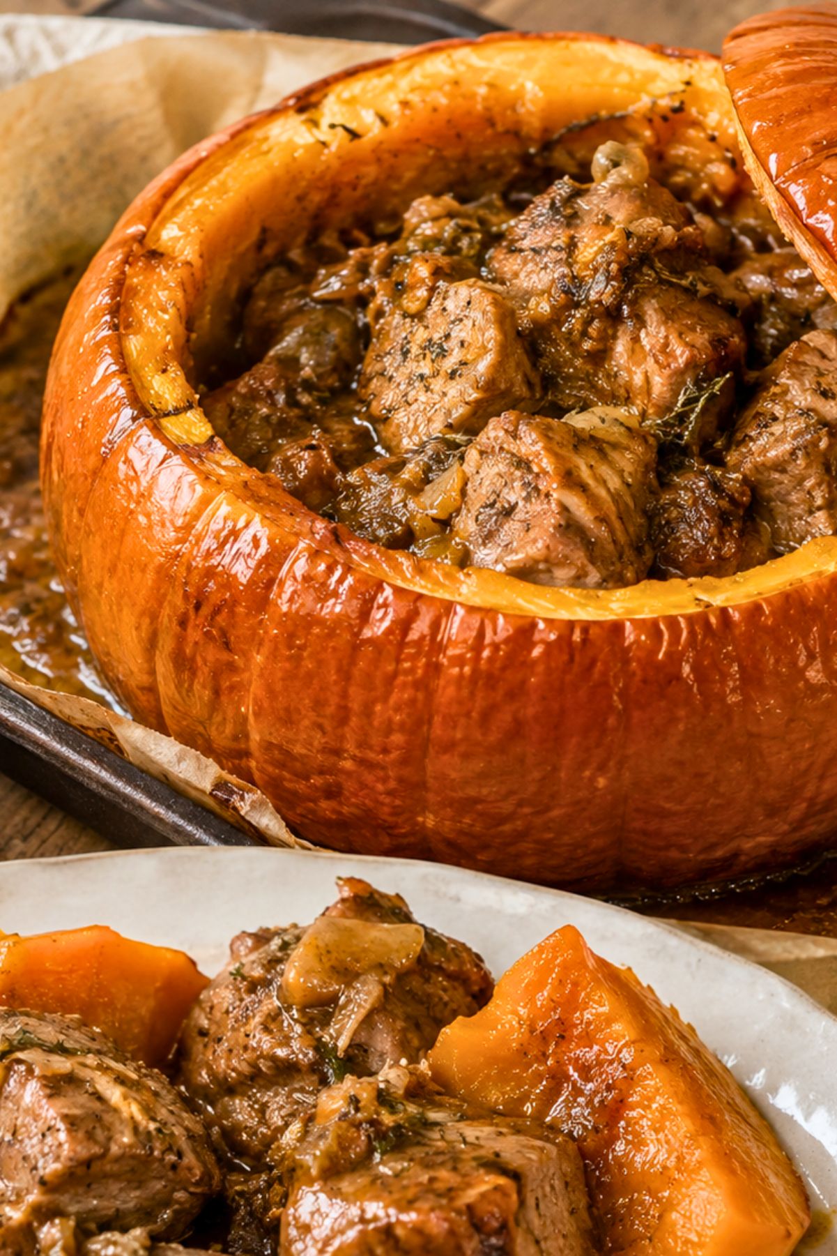 Roasted pumpkin stuffed with tender braised pork in a rich savory sauce, with a serving of pork and roasted pumpkin pieces plated in the foreground.