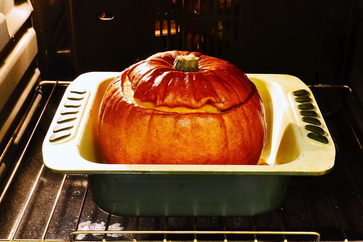 Whole roasted pumpkin with its lid in place, sitting in a roasting pan inside an oven while baking.
