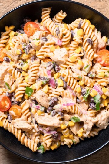 Southwest chicken pasta salad with rotini, chicken, black beans, corn, cherry tomatoes, red onion, cilantro, and creamy dressing in a black bowl.