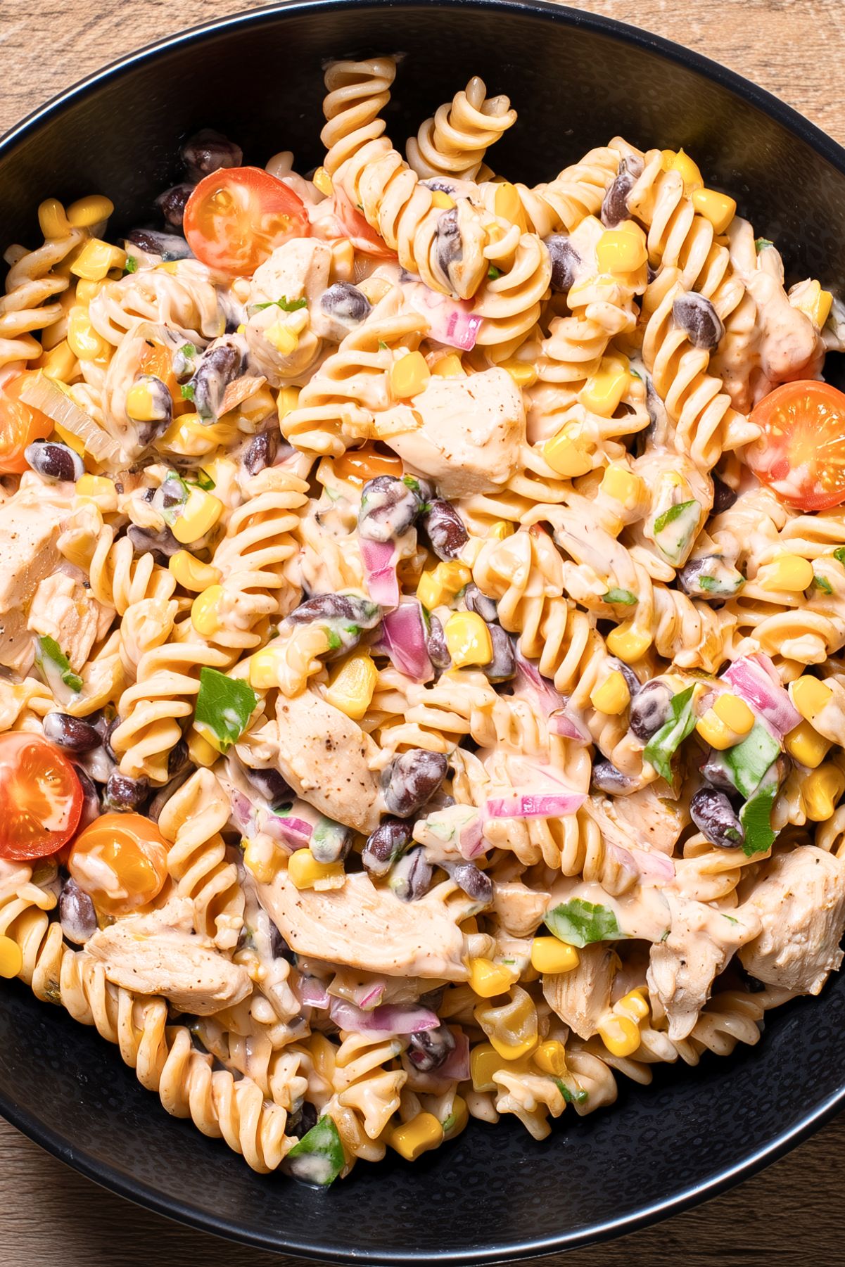 Southwest chicken pasta salad with rotini, chicken, black beans, corn, cherry tomatoes, red onion, cilantro, and creamy dressing in a black bowl.
