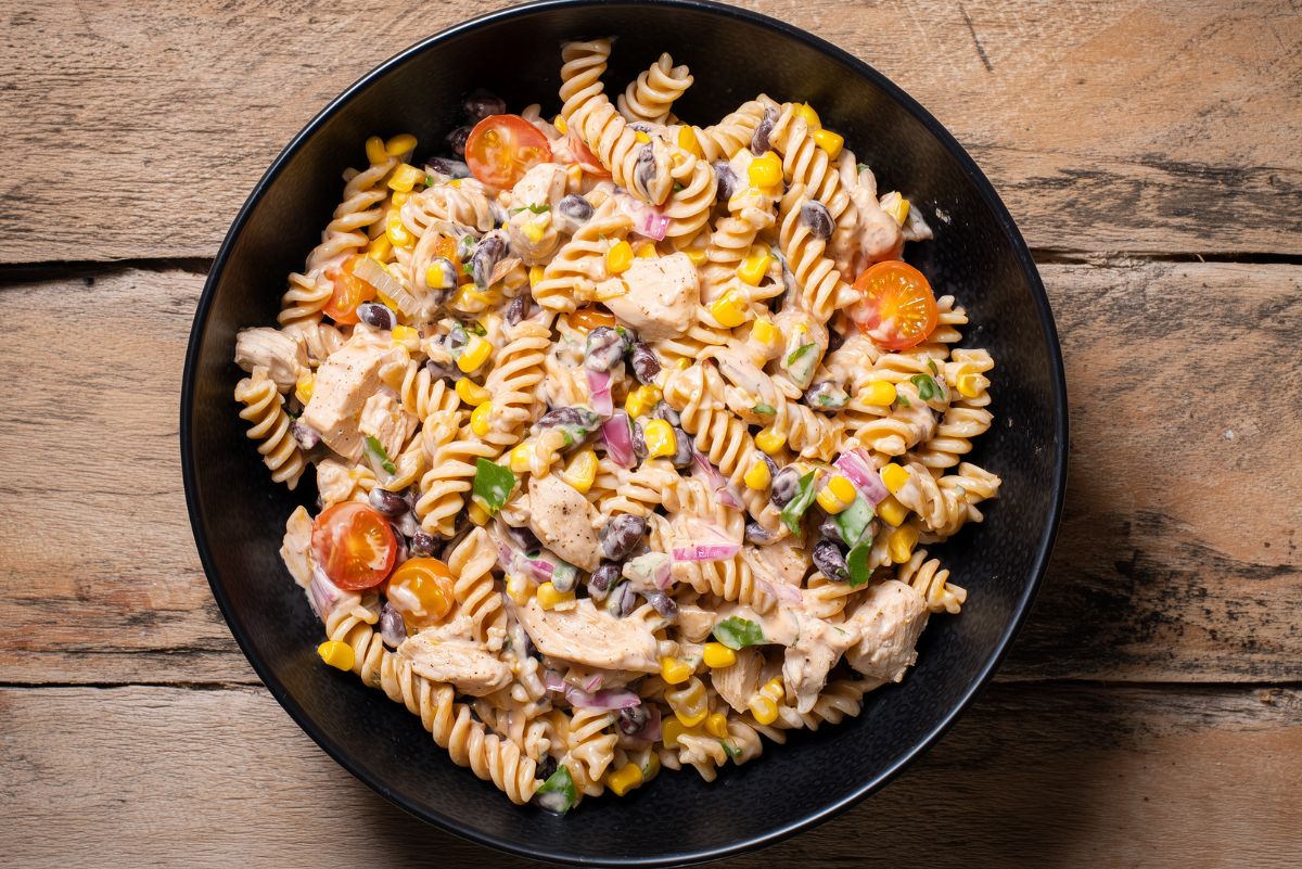 Southwest chicken pasta salad with rotini, chicken, black beans, corn, tomatoes, red onion, cilantro, and creamy dressing in a black bowl on a rustic wooden table.