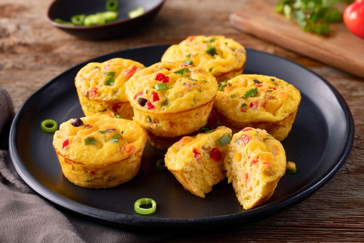 Southwest egg bites with black beans, red bell pepper, green onions, and cheese arranged on a black plate, with one egg bite cut open to show the soft center.
