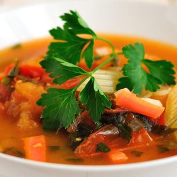Spicy Tomato Trout and Vegetable Soup with chunks of trout, tomatoes, celery, red bell pepper, leafy greens, and fresh parsley in a rich tomato broth.