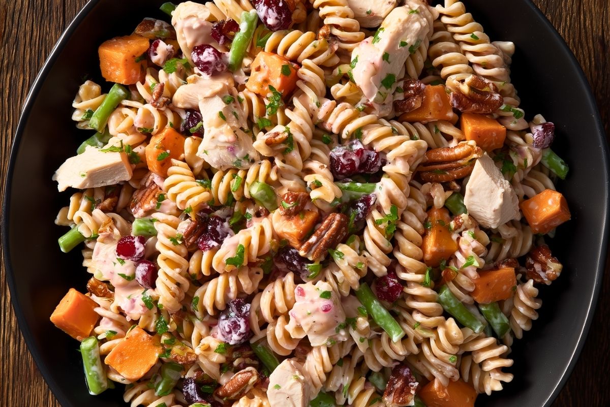 Close-up of creamy Thanksgiving turkey pasta salad with rotini, turkey, roasted sweet potatoes, green beans, cranberries, pecans, and chopped herbs.