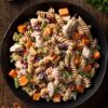 Overhead bowl of Thanksgiving turkey pasta salad with rotini, turkey, sweet potatoes, green beans, cranberries, and pecans on a rustic wood table.
