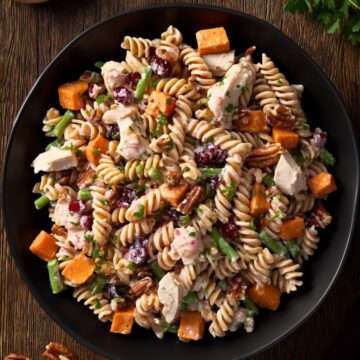 Overhead bowl of Thanksgiving turkey pasta salad with rotini, turkey, sweet potatoes, green beans, cranberries, and pecans on a rustic wood table.