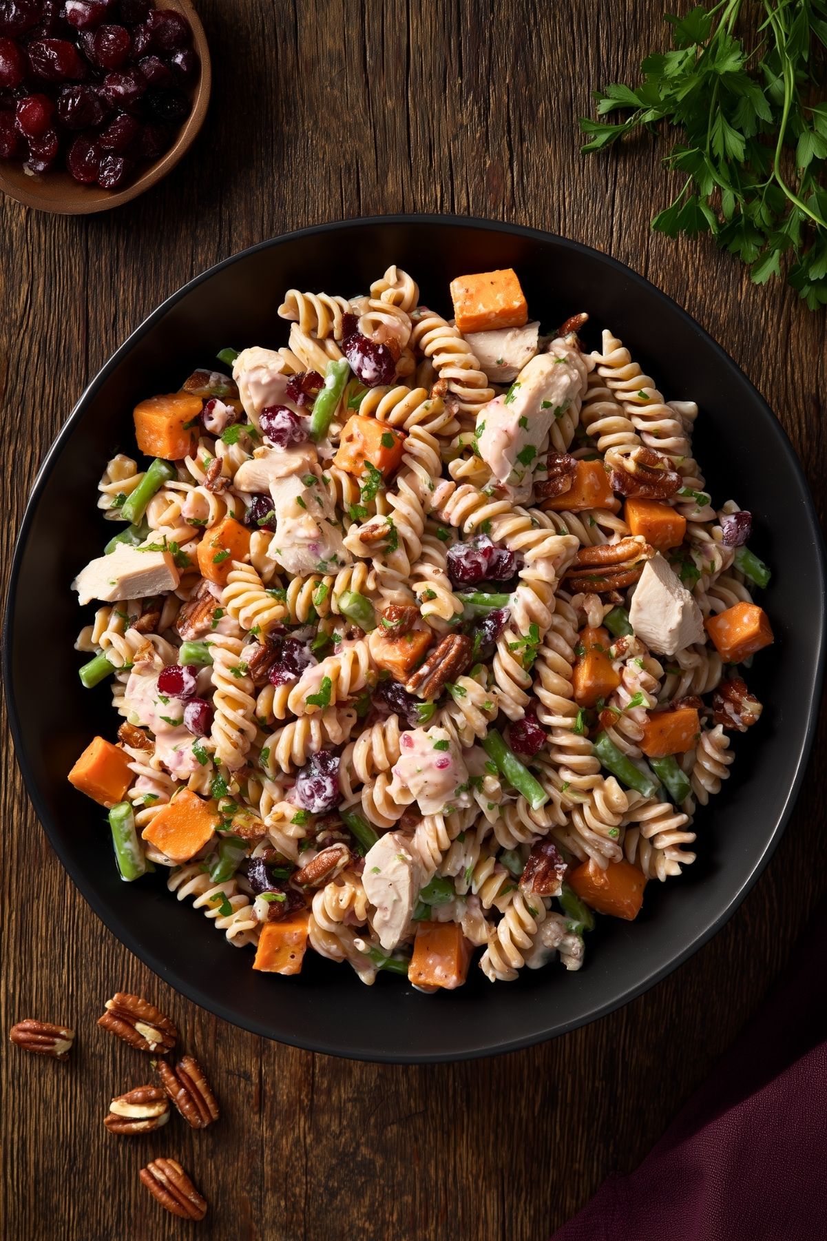 Overhead bowl of Thanksgiving turkey pasta salad with rotini, turkey, sweet potatoes, green beans, cranberries, and pecans on a rustic wood table.