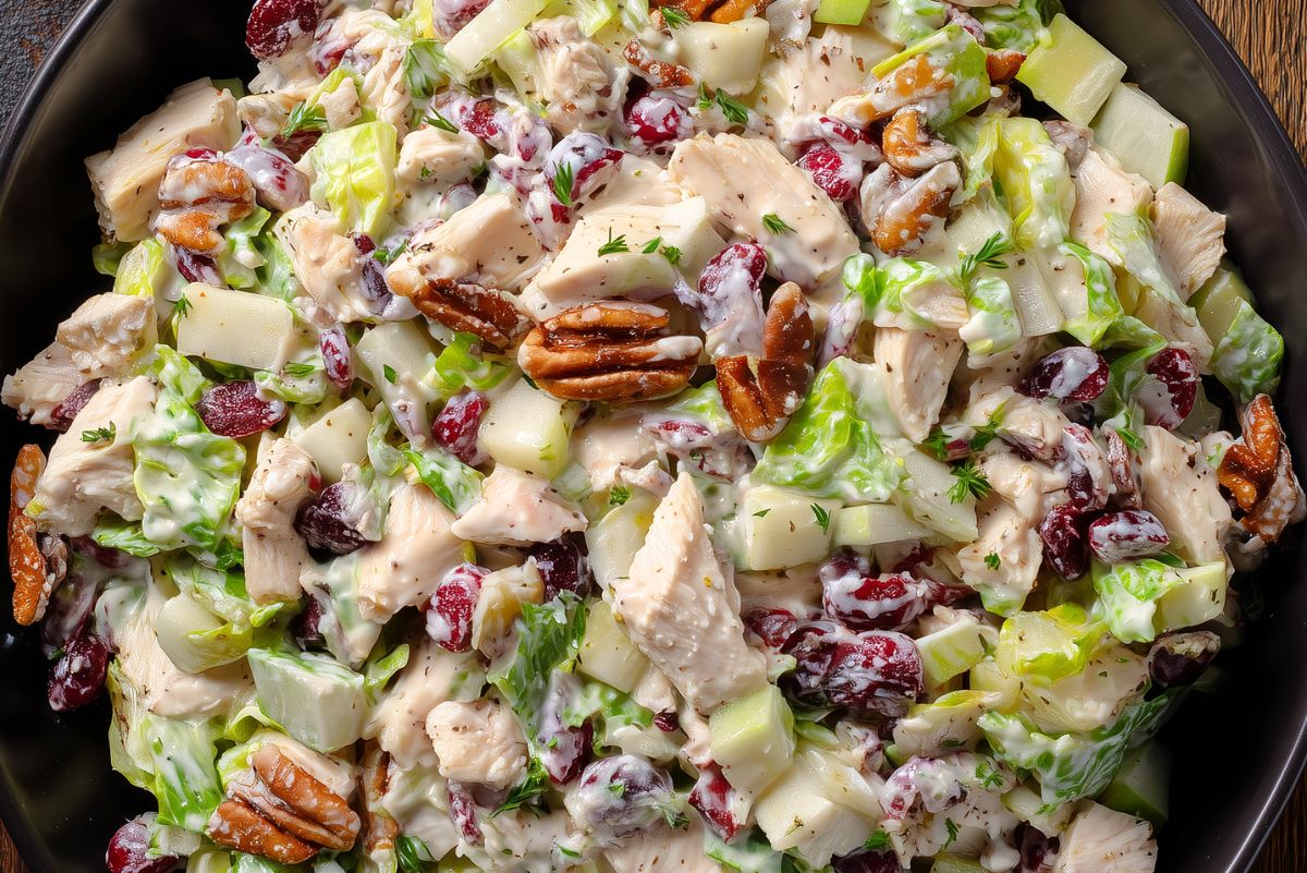 Close-up of creamy turkey cranberry chopped salad with romaine, diced apples, dried cranberries, pecans, and fresh herbs in a black bowl.