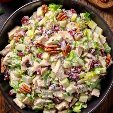 Overhead view of turkey cranberry chopped salad with romaine, turkey, apples, dried cranberries, and pecans in creamy dressing, styled with an apple, fresh cranberries, and pecans on rustic wood.