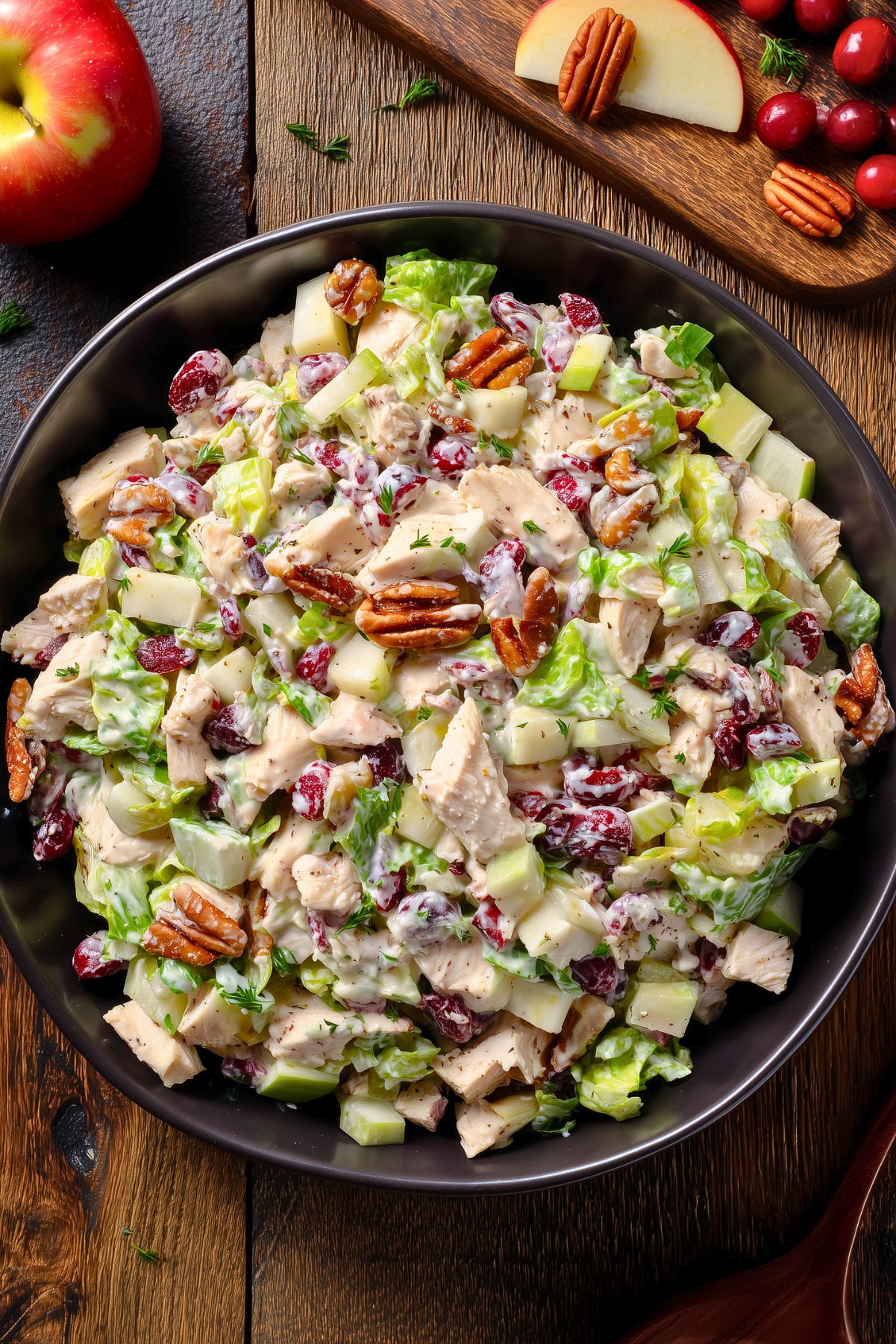 Overhead view of turkey cranberry chopped salad with romaine, turkey, apples, dried cranberries, and pecans in creamy dressing, styled with an apple, fresh cranberries, and pecans on rustic wood.