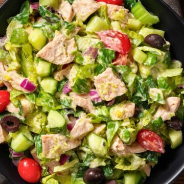 Turkey Grinder Chopped Salad with chopped turkey, romaine lettuce, cucumber, cherry tomatoes, red onion, black olives, and creamy dressing served in a black bowl.