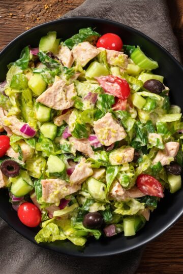 Turkey Grinder Chopped Salad with chopped turkey, romaine lettuce, cucumber, cherry tomatoes, red onion, black olives, and creamy dressing served in a black bowl.