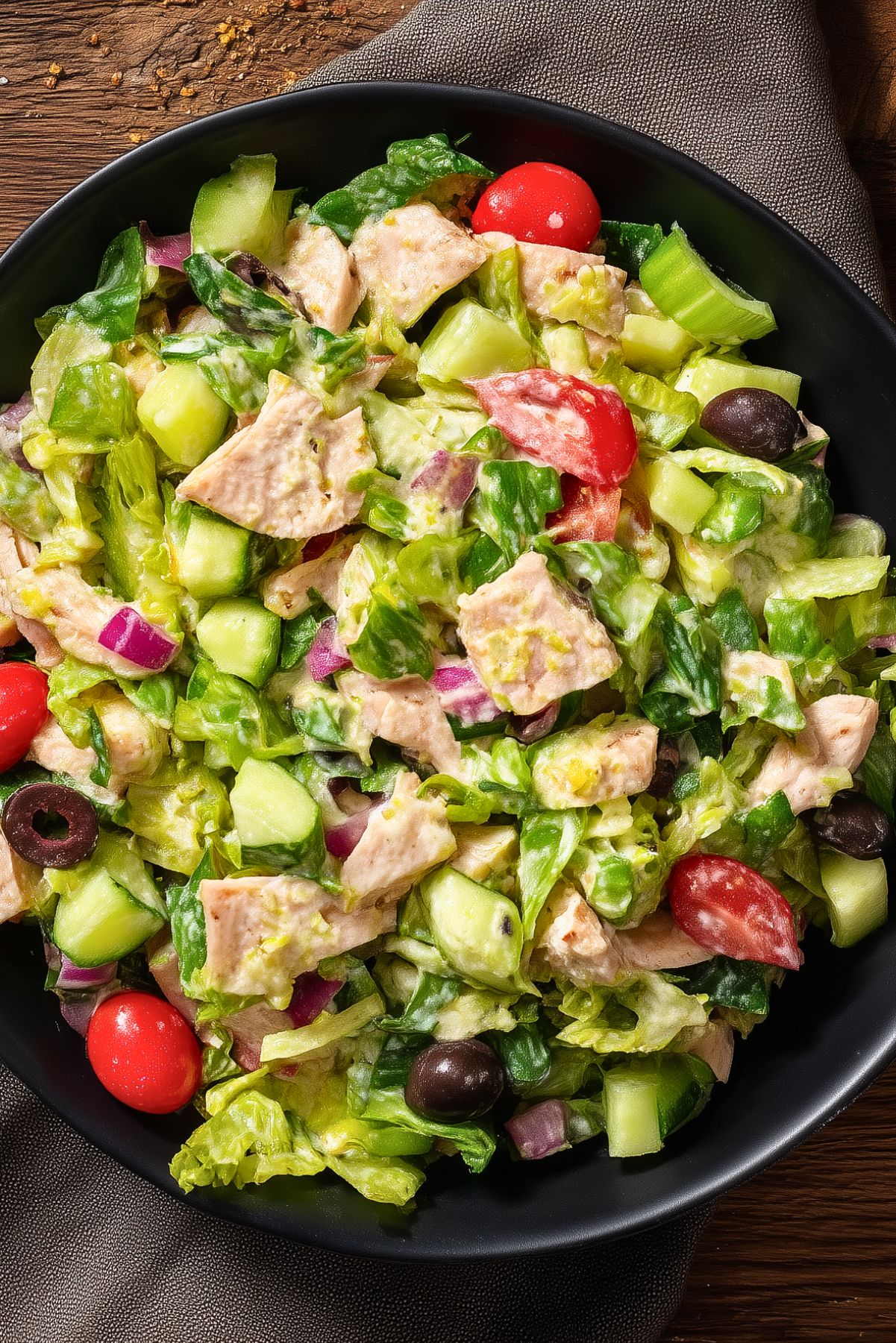 Turkey Grinder Chopped Salad with chopped turkey, romaine lettuce, cucumber, cherry tomatoes, red onion, black olives, and creamy dressing served in a black bowl.