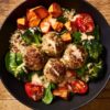Overhead view of a turkey meatball sweet potato bowl with quinoa, roasted broccoli, spinach, tomatoes, and creamy dressing.