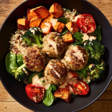 Overhead view of a turkey meatball sweet potato bowl with quinoa, roasted broccoli, spinach, tomatoes, and creamy dressing.