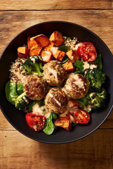 Overhead view of a turkey meatball sweet potato bowl with quinoa, roasted broccoli, spinach, tomatoes, and creamy dressing.