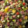 Turkey pepperoni grinder chopped salad with romaine lettuce, cucumber, tomatoes, red onion, banana peppers, black olives, provolone cheese, and creamy Italian dressing in a black bowl.