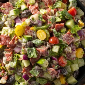 Turkey pepperoni grinder chopped salad with romaine lettuce, cucumber, tomatoes, red onion, banana peppers, black olives, provolone cheese, and creamy Italian dressing in a black bowl.